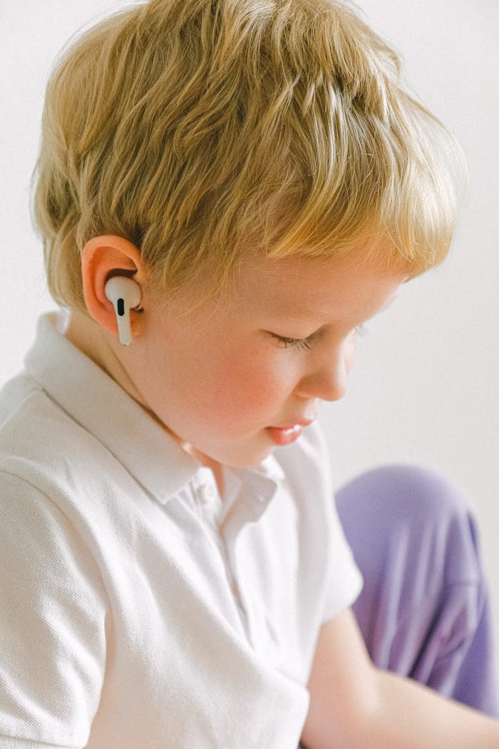 hero-img-02 Adorable blond child wearing wireless earphones, enjoying music indoors.
